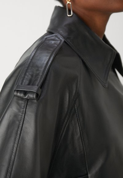 Μαύρο δερμάτινο μπουφάν με δομημένο γιακά, επιγονατίδες στους ώμους και λείο, γυαλιστερό υλικό. Διαθέτει μινιμαλιστικό σχέδιο και ακριβή ραφή.