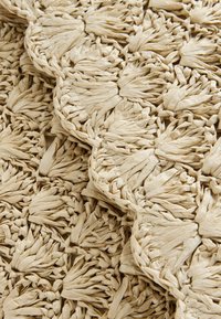 Gewebter Stoff in beige, strukturiert mit Büscheln und Zöpfen, präsentiert komplexe Muster und ein weiches, schichtartiges Aussehen.