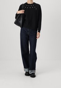 Sudadera negra con detalles de ojales plateados en el pecho, combinada con jeans de mezclilla anchos de color azul y zapatos negros tipo slip-on.