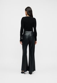 Μαύρο εφαρμοστό πουλόβερ σε συνδυασμό με ψηλόμεσα, φαρδιά μαύρα παντελόνια από δερματίνη. Απαλή υφή, ελάχιστες λεπτομέρειες και ραμμένη σιλουέτα.