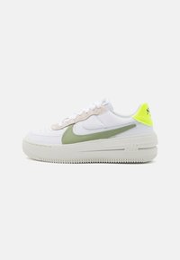Zapatillas de piel blanca con un swoosh verde claro, acentos de ante beige y una lengüeta en neón amarilla; cuentan con una suela blanca gruesa.