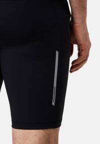 Shorts de sport noirs au design ajusté, en matériau extensible. Caractéristiques d'un logo argenté réfléchissant et d'accents sur les côtés. Texture lisse.