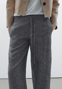 Dark gray linen trousers with a loose fit, drawstring waist, and side pockets. Subtle texture with a casual design.