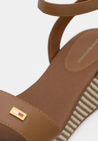 Brown wedge sandal featuring two slim straps, a gold accent, and a textured checkered pattern on the sole. Smooth matte finish.