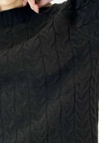 Suéter negro de punto con un patrón de trenzas, cuello redondo y puños acanalados. La textura parece suave y gruesa.