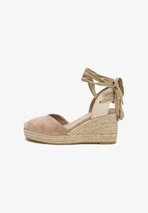 Zapato de cuña de ante beige con correas en el tobillo decoradas, plantilla de yute trenzado y un diseño de punta redondeada. El tacón mide aproximadamente 7 cm.