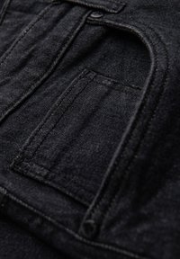 Tissu en denim noir avec une finition texturée, comprenant une poche avec des coutures visibles et un bouton rond en haut.