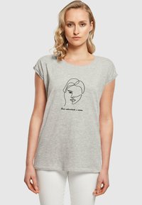 Grå kortærmet t-shirt lavet af blødt stof, med en sort stregtegning af et ansigt og tekst nedenunder i en buet skrifttype.
