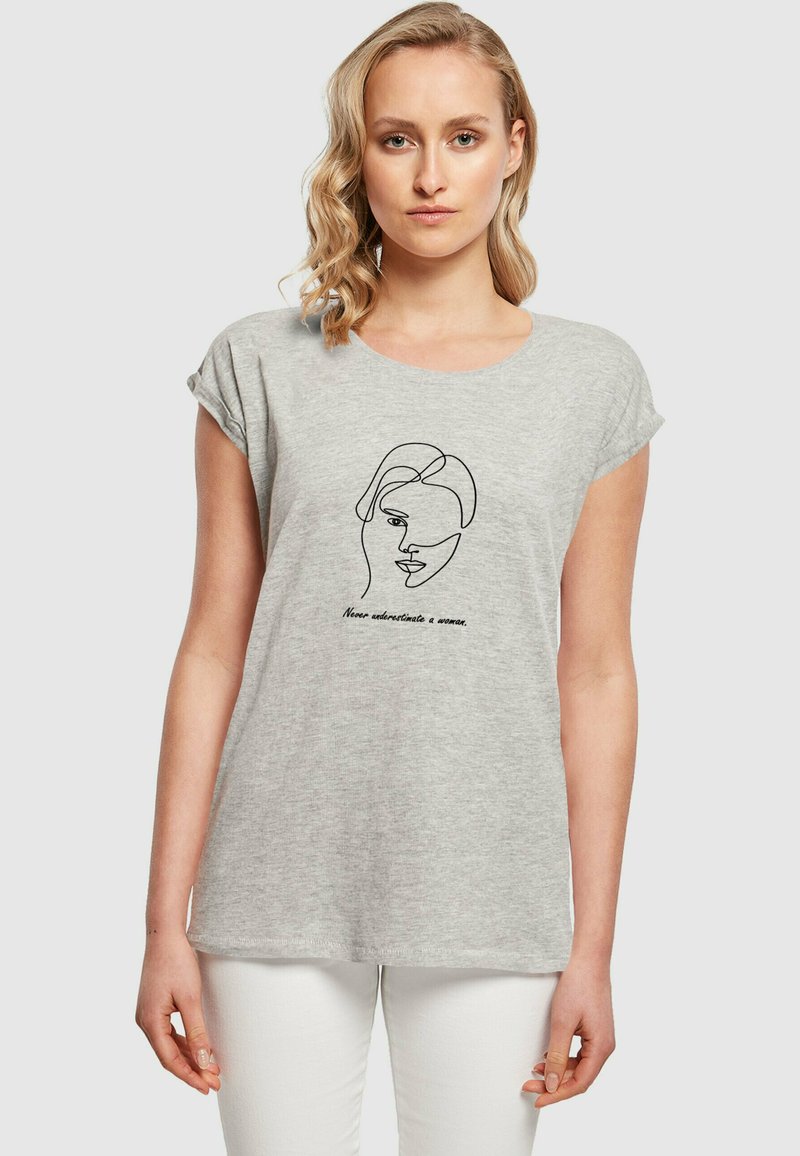 Grå kortærmet t-shirt lavet af blødt stof, med en sort stregtegning af et ansigt og tekst nedenunder i en buet skrifttype.