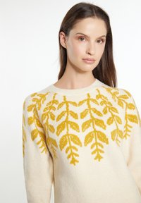 Pulover crem cu modele de frunze galbene, guler rotund și mâneci lungi. Textura pare moale și tricotată, cu un finisaj confortabil.