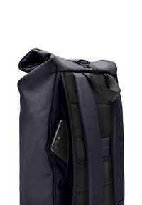 Sac à dos bleu marine avec un extérieur texturé, des bretelles rembourrées et un compartiment zippé révélant un smartphone noir à l'intérieur.