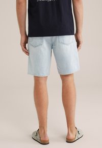 Gai zili džinsu šorti ar brīvu piegriezumu, ar divām aizmugurējām kabatām un taisnu apakšmalu. Valkāti ar pelēkām slīdējošām kurpēm.