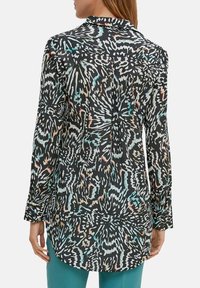 Chemise à manches longues avec un fond noir, ornée d'un motif abstrait coloré en bleu sarcelle et orange. Tissu doux, col rabattu et ourlet incurvé.