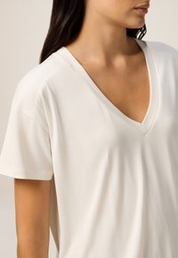 Cremfarbendes V-Ausschnitt-T-Shirt aus weichem Stoff, mit kurzen Ärmeln und einem lässigen Schnitt. Glatte Textur mit minimalen Nähdetails.