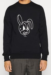 Felpa nera con un grande design di coniglio in stile cartone animato di colore bianco sul davanti. Collo e polsini a costine, tessuto morbido in misto cotone.