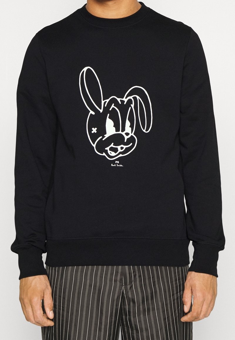 Felpa nera con un grande design di coniglio in stile cartone animato di colore bianco sul davanti. Collo e polsini a costine, tessuto morbido in misto cotone.