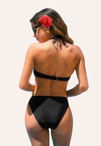 Zwarte bikini met een haltertop en hoge taille broekjes. Gladde textuur, minimalistisch ontwerp, zilveren hardware en een bloemen haaraccessoire.