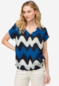 Blusa a maniche corte con un motivo a zigzag blu, blu navy e bianco. Tessuto leggero con scollatura a V e dettaglio alla vita elasticizzato.