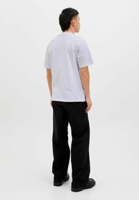 Vaaleanharmaa puuvillapaita, jossa on rento istuvuus ja lyhyet hihat, yhdistetty mustiin housuihin ja mustiin kenkiin. Yksinkertainen muotoilu, ilman näkyviä kuvioita.