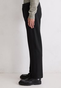 Un pantalon noir à coupe droite, avec une texture de tissu lisse et des poches latérales, associé à des chaussures à lacets noires.