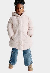 Piumino rosa chiaro con cappuccio, caratterizzato da un design trapuntato. Abbinato a jeans a gamba larga blu con dettagli floreali e sneakers marroni chiaro.