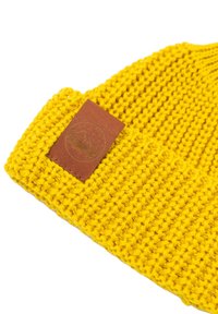 Żółta czapka z dzianiny o fakturowanym materiale. Posiada brązową skórzaną naszywkę z logo, z widocznymi prążkowymi detalami wzdłuż krawędzi.