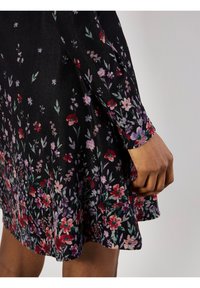Abito nero con motivo floreale in rosso, viola e verde. Maniche lunghe e orlo svasato. Il tessuto ha una finitura testurizzata.