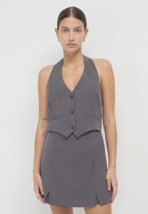 Haut en halter gris avec une silhouette ajustée, présentant un décolleté en V et quatre boutons, associé à une mini jupe assortie avec des fentes sur les côtés.