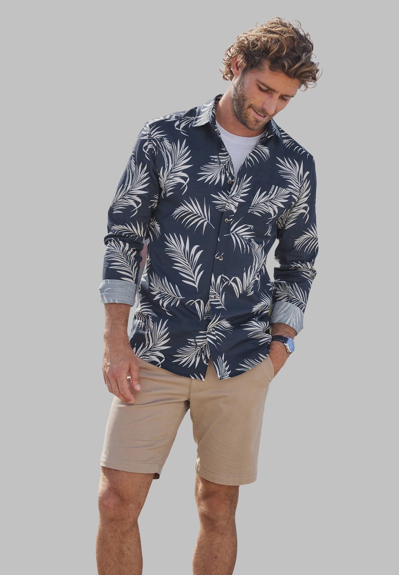 Marineblauw overhemd met witte palmenbladpatroon, opgerolde mouwen, gecombineerd met beige shorts, casual fit met een subtiele textuur.