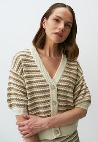 Gestreifter Kurzarm-Cardigan in Creme und Beige mit V-Ausschnitt, ausgestattet mit drei Knöpfen und einem strukturierten Strickmuster.