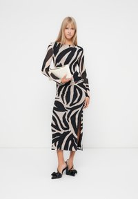 Robe à manches longues avec un imprimé zèbre noir et beige, silhouette ajustée, fente sur le côté, accompagnée de chaussures à talons noires et d'une pochette crème.