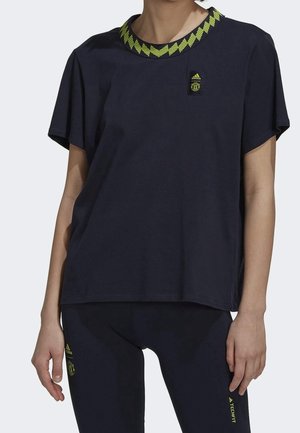 Osoba nosząca czarną sportową koszulkę Adidas z żółto-zielonym kołnierzem w zygzak i pasujące czarne legginsy z logo Adidas.