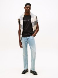 Μαύρο κοντομάνικο T-shirt με την ένδειξη "TOMMY HILFIGER EST. 1985" σε λευκό χρώμα, συνδυασμένο με ανοιχτό μπλε τζιν και ένα γκρι και κρεμ ριγέ πουλόβερ draped στους ώμους.