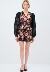 Blomster-mønstrets sort kjole med lange gennemsigtige ærmer, v-hals og knapdetaljer; har en peplum talje og rynket kant.