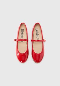 Scarpe Mary Jane in pelle verniciata rossa con punta arrotondata, suola piatta e cinturino regolabile, dotate di una soletta beige con la scritta "BIANCO".