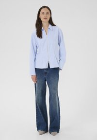 Lyseblå, stribet skjorte med lynlås foran, kombineret med viddebetonede denimbukser. Outfittet har lange ærmer og en løs pasform.