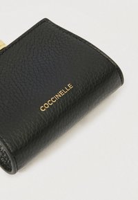 Μαύρο πορτοφόλι από υφή δέρματος με ανάγλυφο χρυσό λογότυπο. Συμπαγές σχέδιο με στρογγυλεμένες άκρες, φινιρισμένο με διακριτικές λεπτομέρειες ραφής.