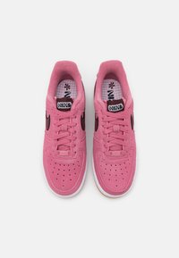 Paire de baskets Nike roses avec logos swoosh noirs, lacets et semelles blanches vues de dessus sur fond blanc.