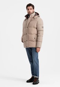 Beige, puffjacka med hög krage, knappar fram och sidfickor. Inuti har den ett rutmönster. Matchad med blåjeans och svarta kängor.