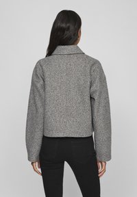 Szara kurtka z mieszanki wełny o skróconym kroju, dużym kołnierzu i szerokich rękawach. Tekstura wydaje się miękka z delikatnym wzorem plamek.