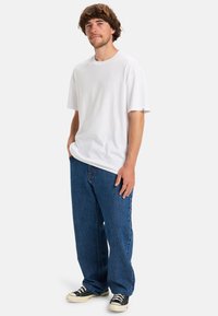 Bílý bavlněný tričko s krátkým rukávem, zkombinované s volnými modrými džíny. Černobílé plátěné tenisky dokončují outfit.