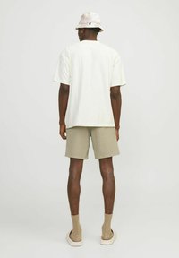 Brīvi pieguļošs, gaiši beigu tekstūrēts īsu piedurkņu krekls, apvienots ar līdz ceļgaliem garām gaiši khaki šortiem. Mīksta, elpojoša auduma; redzama cepure ar platām malām.