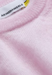 Tissu tricoté rose doux avec étiquette "ARMEDANGELS" et petite étiquette jaune indiquant le matériau mohair.