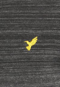 Colibri jaune brodé sur un fond de tissu texturé gris foncé, centré et détaillé.