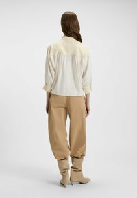 Cream blouse with textured yoke, long puff sleeves, and buttoned cuffs. Paired with beige high-waisted pants and beige heeled boots.