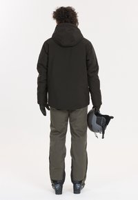 Ski jakke i mørkebrun, parret med olivengrønne ski bukser. Jakken har hætte, og outfittet inkluderer handsker og en grå hjelm.