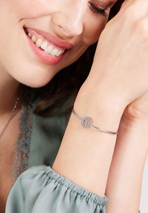 Zilveren armband met een ronde bedel met een ovale uitsparing, gedragen om een pols. Het model draagt een zachte, gestructureerde groene blouse.