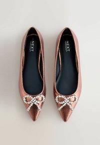 Ballet flats en or rose, à bout pointu avec une finition texturée, ornées d'un nœud décoratif embellit de pierres précieuses transparentes à l'avant.