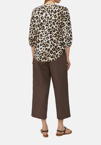 Bluse mit Leopardenmuster und Dreiviertelärmeln, kombiniert mit braunen, weiten Hosen. Die Bluse hat einen abgerundeten Saum und besteht aus einem leichten Stoff.