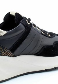 Baskets noires en cuir et daim, avec une semelle blanche épaisse, des œillets dorés et un accent en maille texturée sur le côté.
